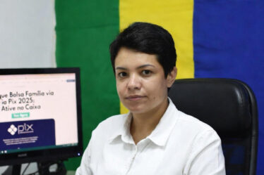 Mulher em escritório consulta saque Bolsa Família via Pix 2025 no Caixa Tem com bandeira do Brasil ao fundo